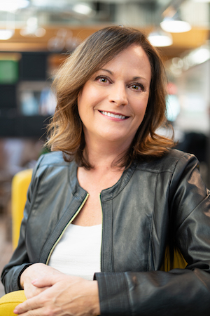 A woman in a leather jacket smiling in an office.